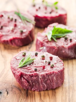 Fresh beef fillets seasoned with herbs and spices on a wooden cutting board, ideal for grilling or cooking.