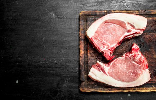 Raw pork chops on a wooden cutting board, showcasing fresh meat ready for preparation and cooking.